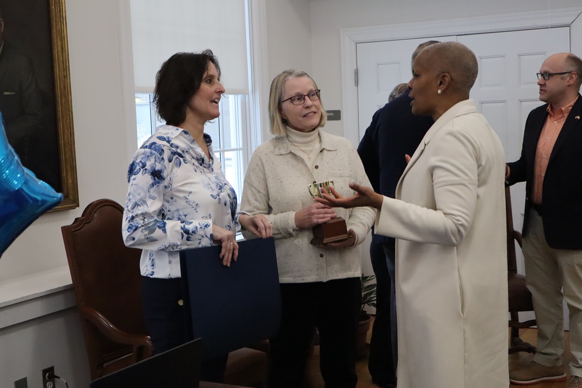 The three women speak while Thomas gestures with both hands.