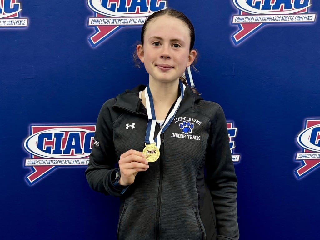 Chase Gilbert poses with her medal in front of a CIAC logo backdrop at the meet.