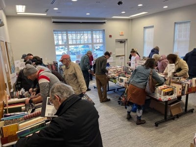 About 17 people browse stacks set up along the wall and at a center table in the Community Room.