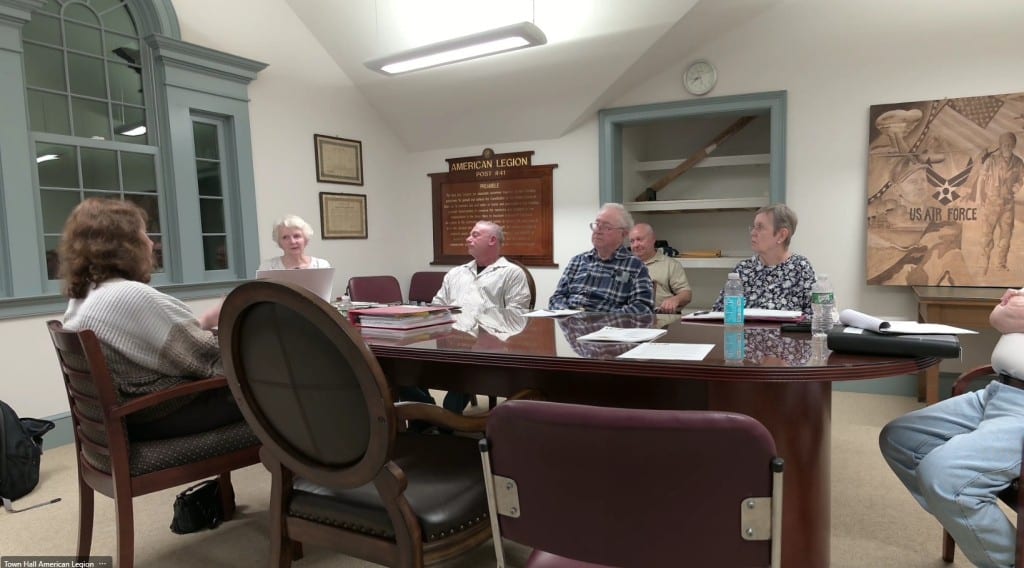 Members sit around an oval table almost as big as the room. 