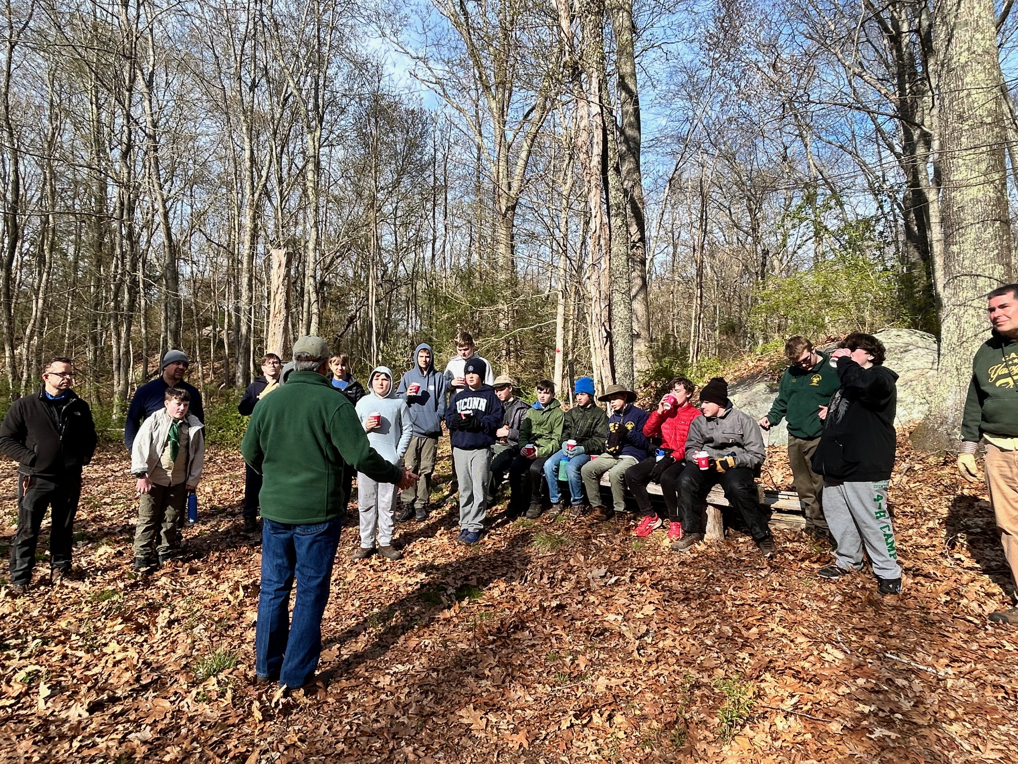 A man in a green fleece jacket stands in front of members of the Boy Scout troop, some of whom are drinking from red cups.