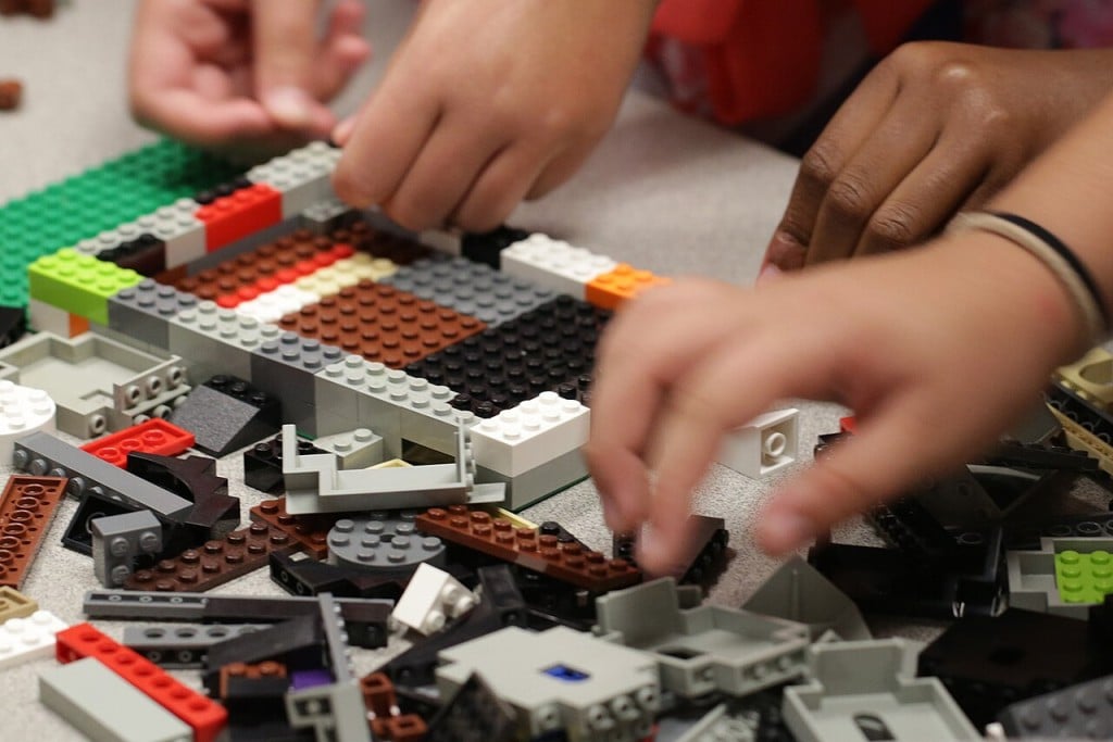 a pile of LEGOS with hands visible piecing them together. 