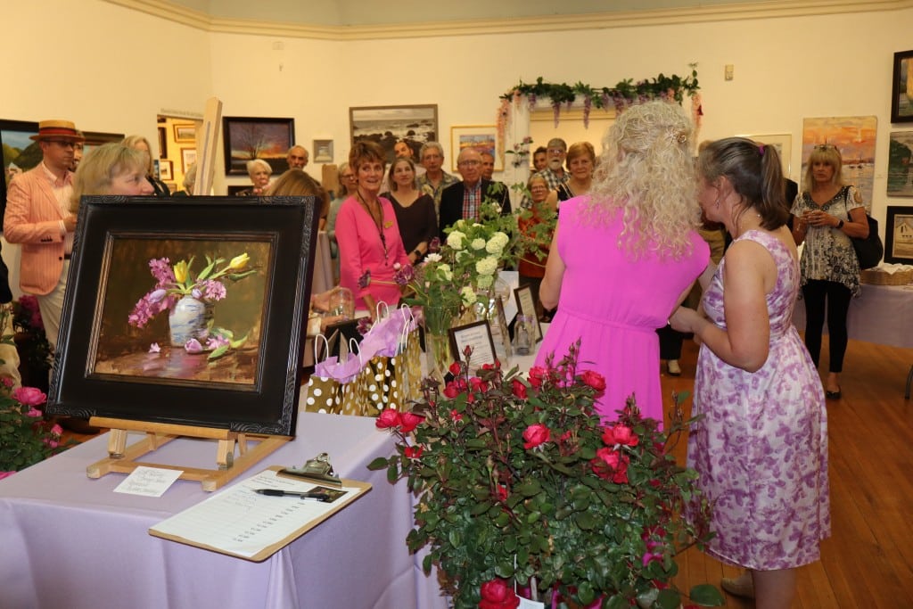 Attendees gather around the raffle table with the silent auction prize, a framed painting of a bouquet, at the front.