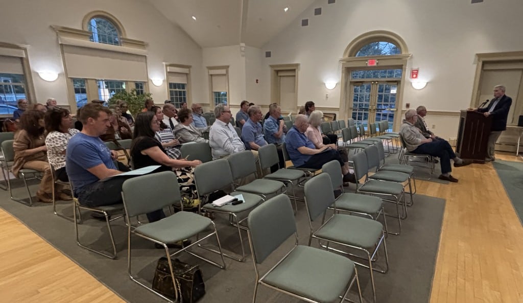 Voters in chairs in the meeting room look at the moderator.