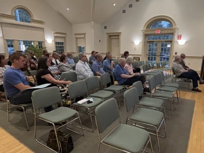 Voters in chairs in the meeting room look at the moderator.