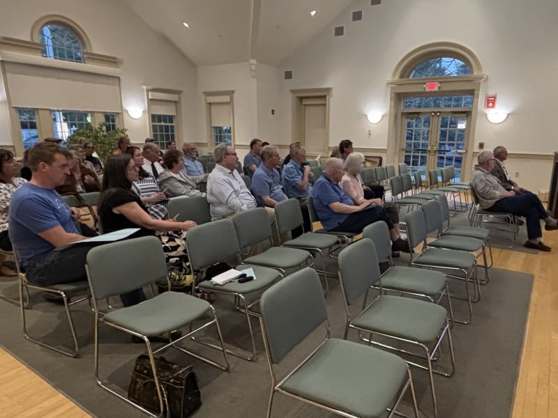 Voters in chairs in the meeting room look at the moderator.
