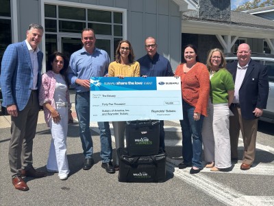 Eight people stand with a large check resting on two Meals on Wheels tote bags.