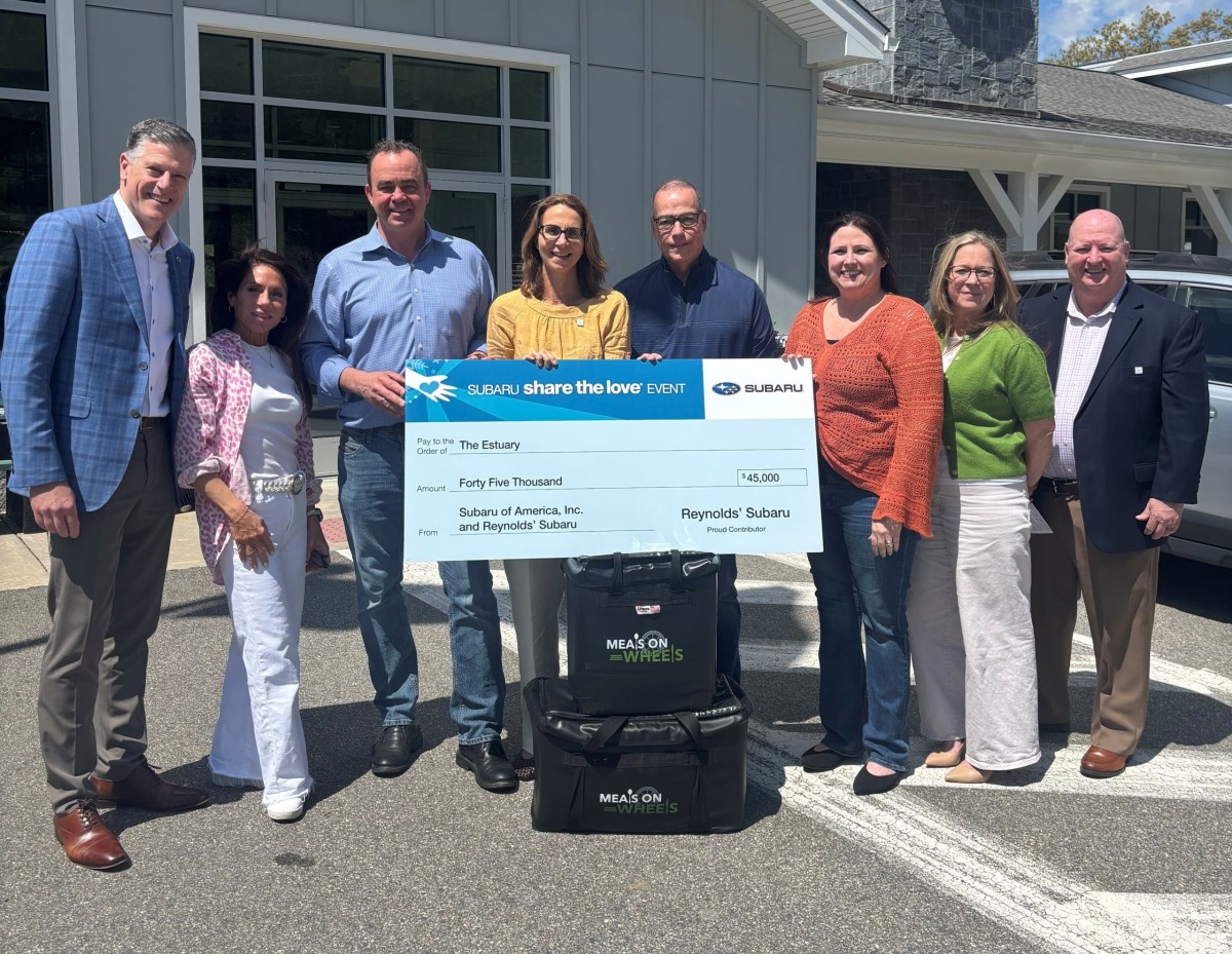 Eight people stand with a large check resting on two Meals on Wheels tote bags.