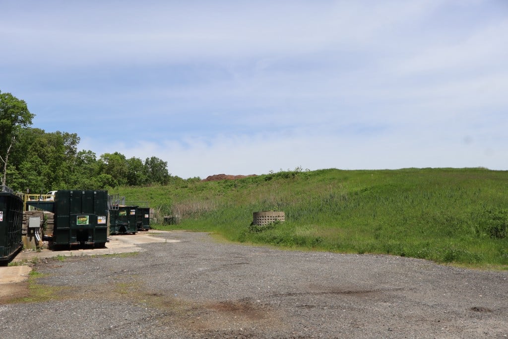 A hilly expanse rising up from a road with dumpsters along it.