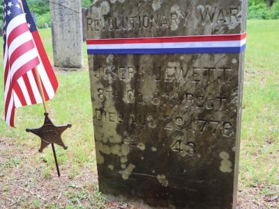 An hisotric gravestone next to a flag affixed to a star emblazoned with "1776"