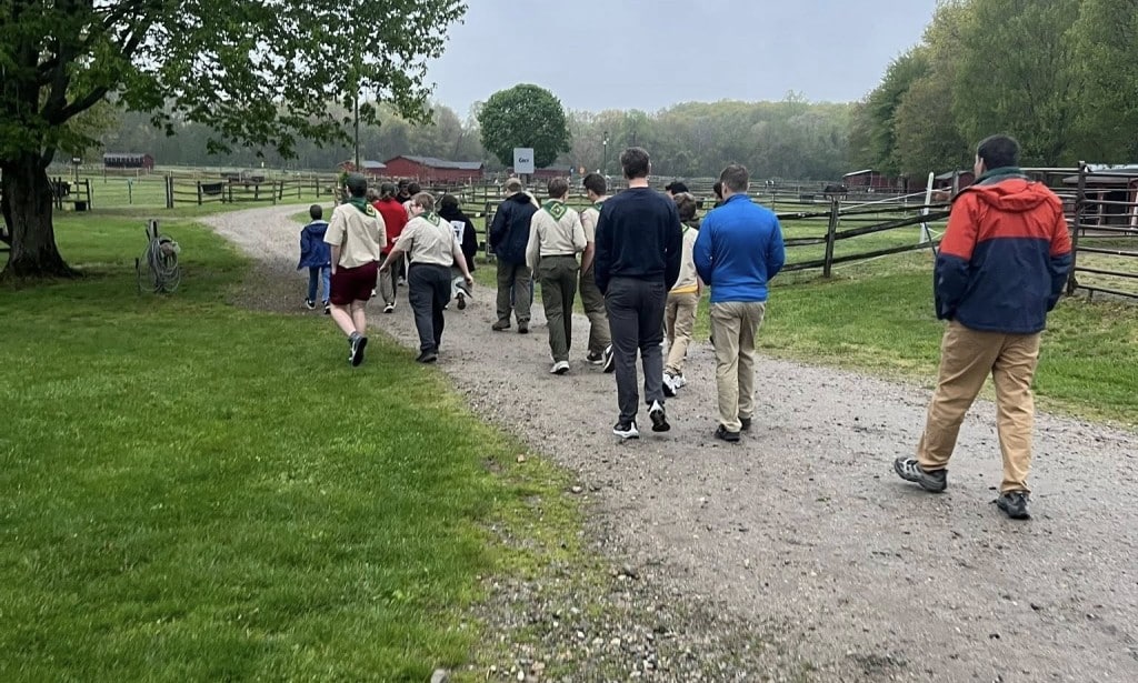 Boys walk on a dirt path between horse paddocks. 