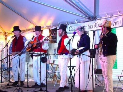 Three men and one women perform on stage in early 1800s clothing