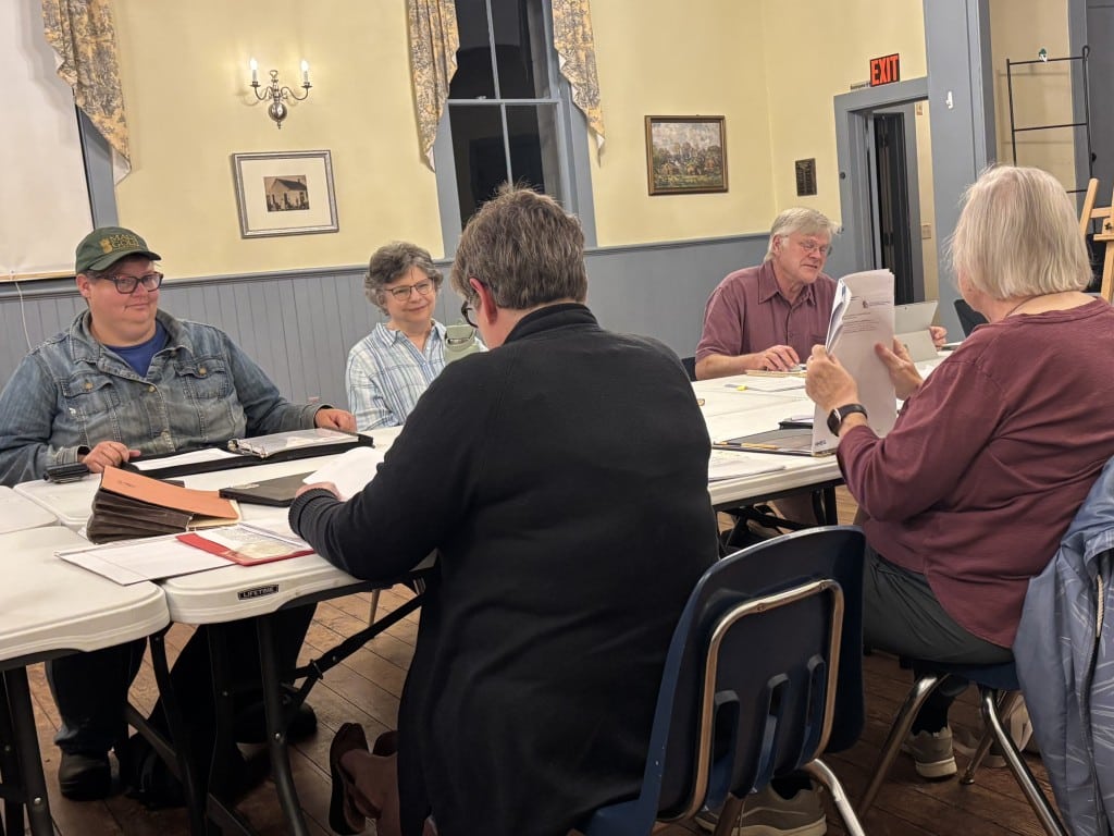 Members sit around a table. 