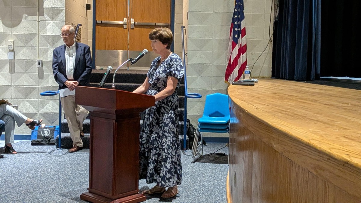 A woman speaking at a podium in a school auditorium