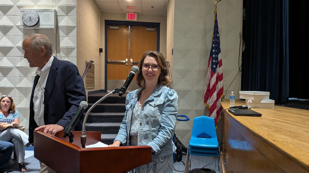 a woman standing at a microphone in a school auditorium