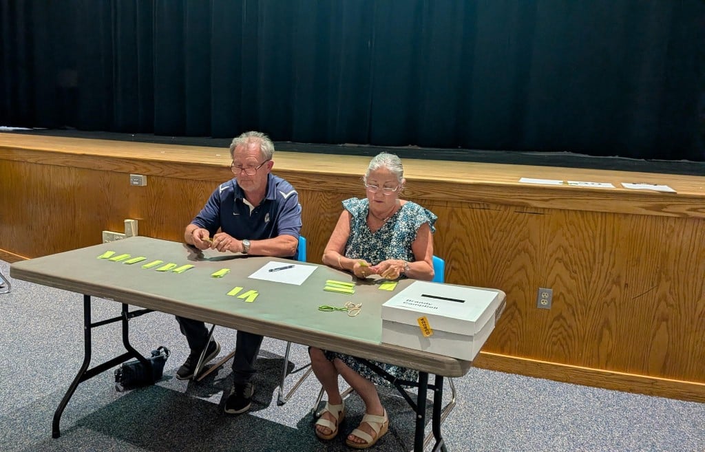 a man and a woman sitting at a table opening and counting ballots.