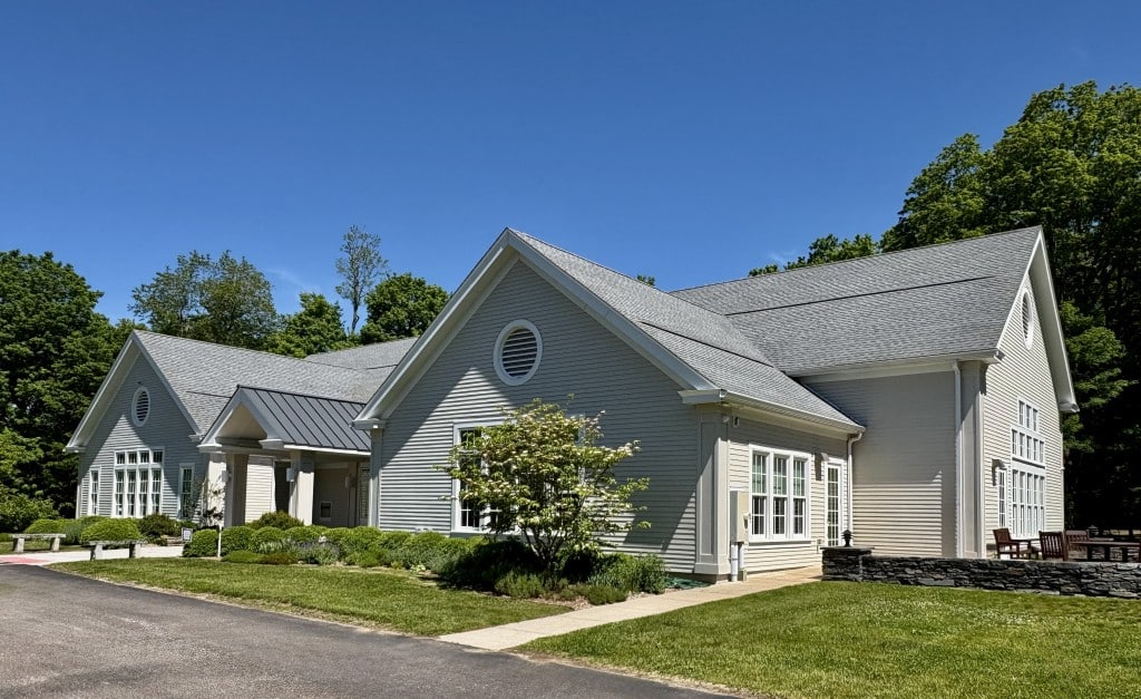 a grey buidling with a tree and garden in front and blue sky