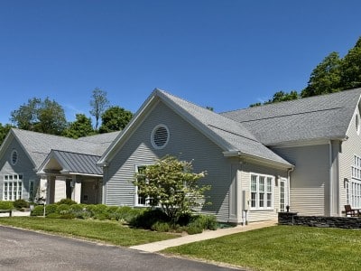 a grey buidling with a tree and garden in front and blue sky