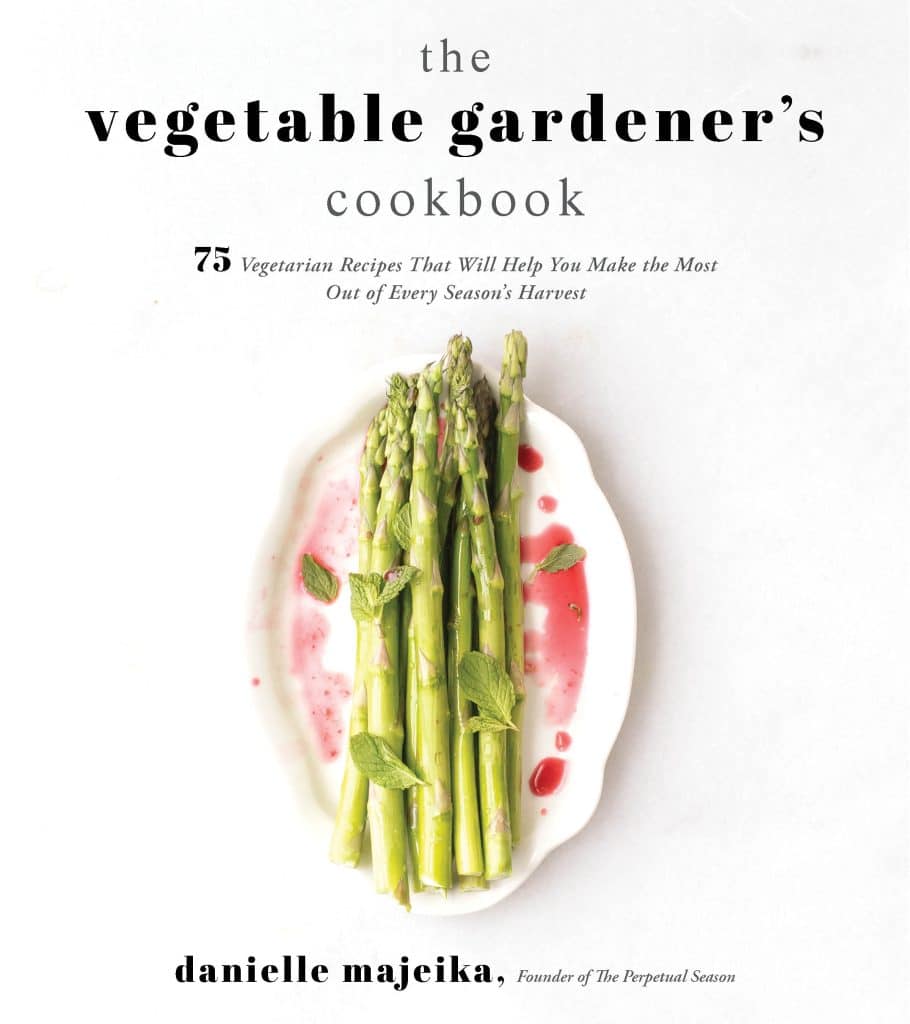 cover of a cookbook with asparagus on a white page drizzled with red sauce and herbs